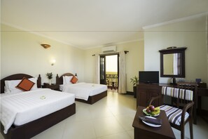 A hotel room with two beds, a desk with a chair, a television, and a dining table with fruit. - Sovan Mealea Hotel (Siem Reap)