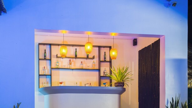 A poolside bar area with a counter, shelves with bottles, hanging lights, and potted plants. - Sovan Mealea Hotel (Siem Reap)