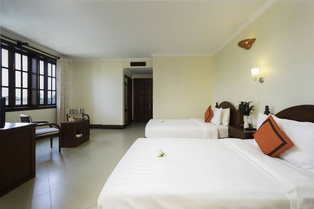 A hotel room with two beds, a desk, a chair, and a window with curtains.