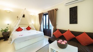 A bedroom with a bed, a nightstand, a sofa, a potted plant, and a wall-mounted air conditioner. - Sovan Mealea Hotel (Siem Reap)