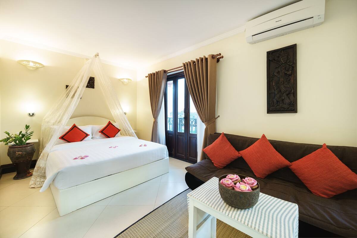 A bedroom with a bed, a nightstand, a sofa, a potted plant, and a wall-mounted air conditioner.