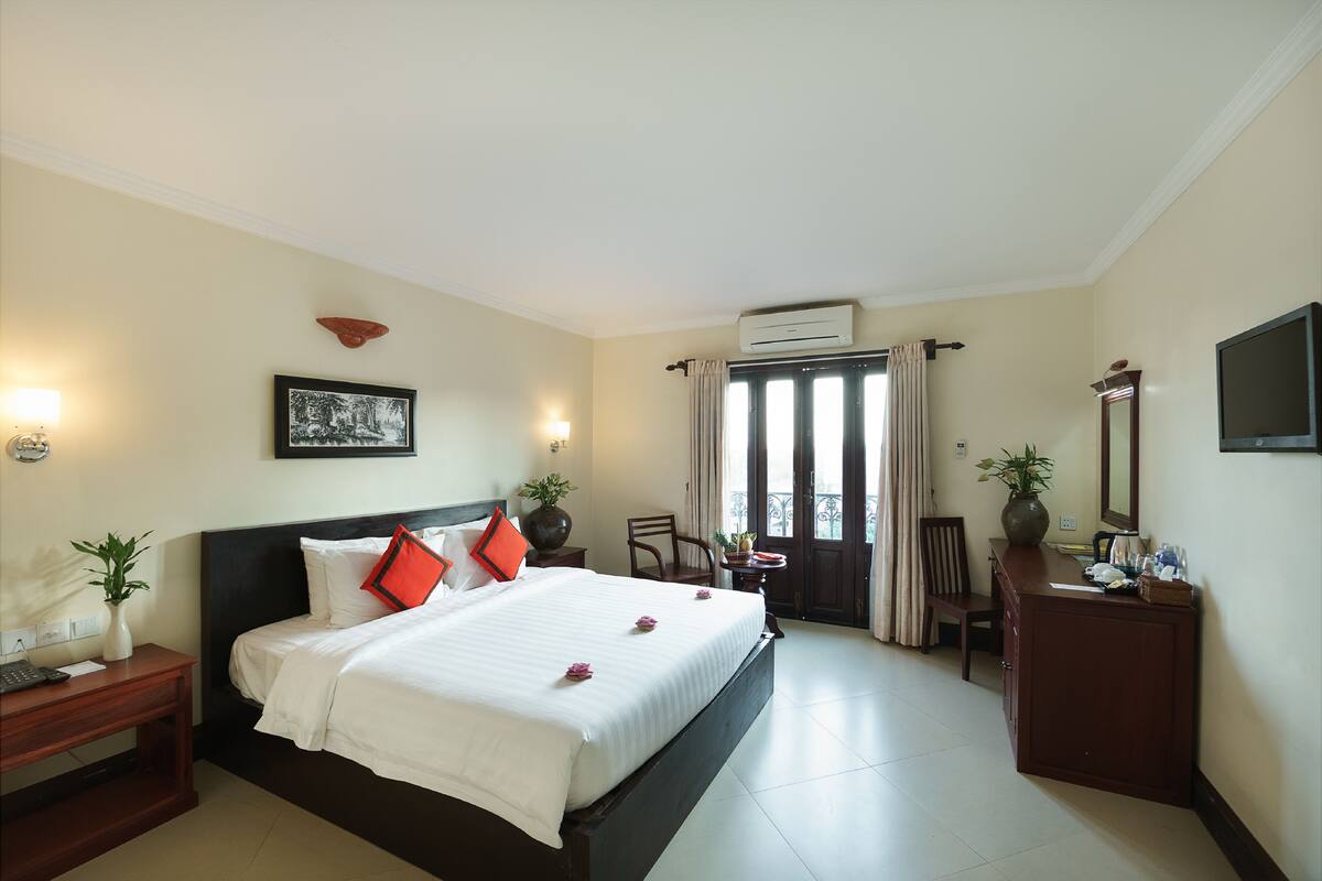 A hotel room with a bed, bedside table, desk, chair, and a large window with curtains.