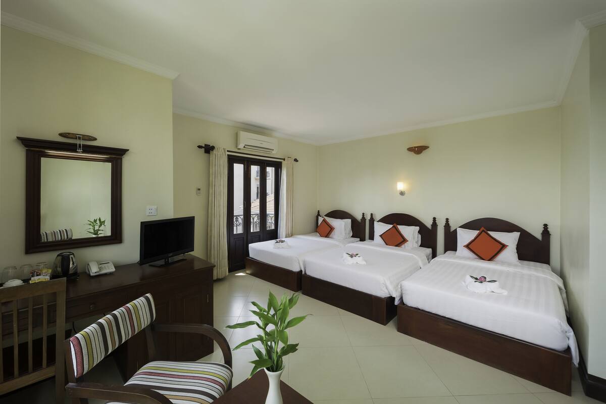 A hotel room with two beds, a desk, a television, and a window with curtains.