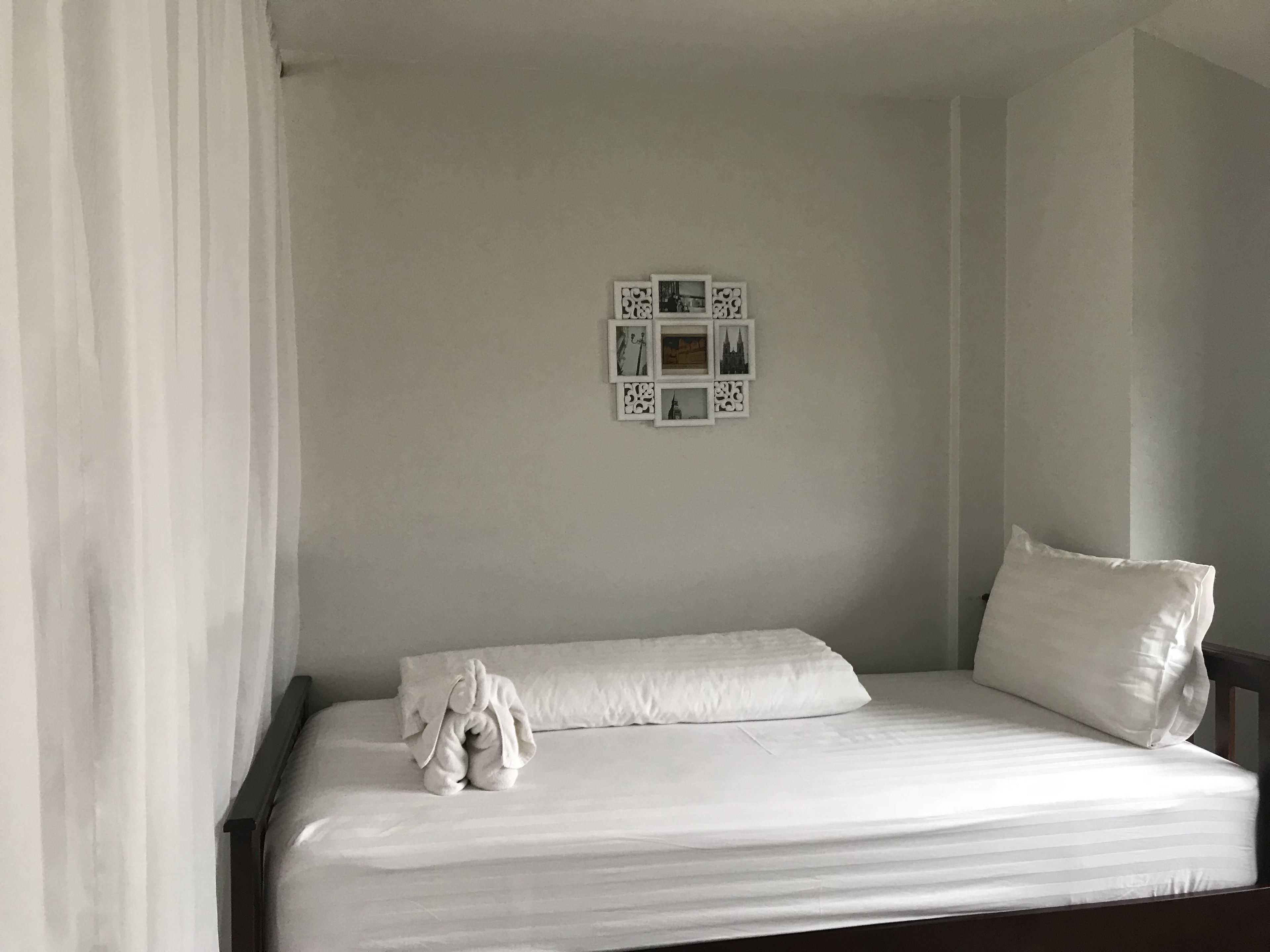 A single bed with white linens, a headboard, and a pillow. There are framed pictures on the wall above the bed.