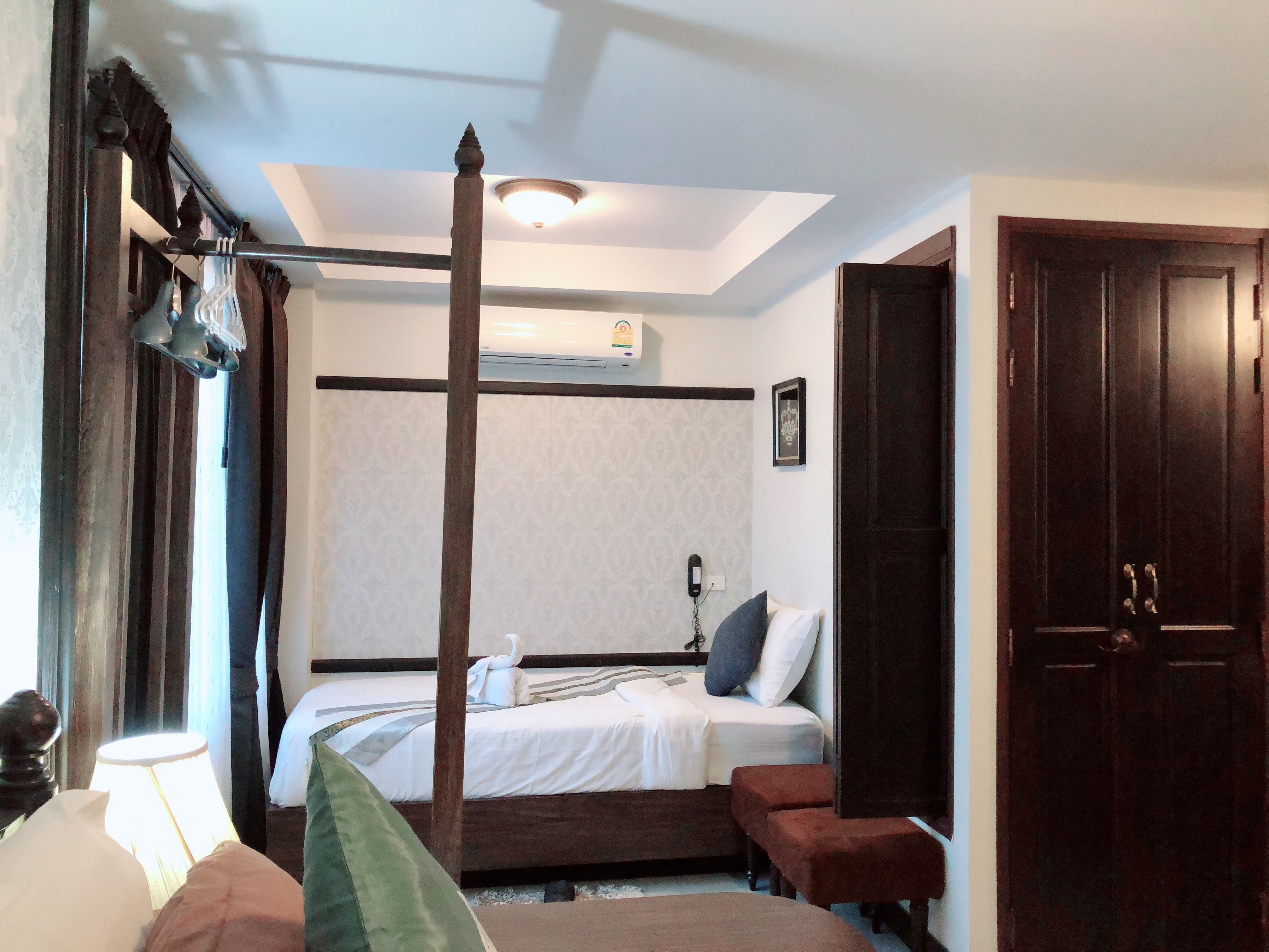Een slaapkamer met een hemelbed, nachtkastje, lamp, garderobe en plafondlamp.