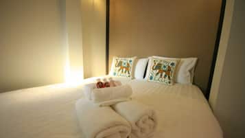 Una cama bien hecha con sábanas blancas, dos almohadas decorativas y un juego de toallas.