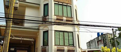 Un edificio de dos pisos con un balcón en el nivel superior y una entrada cubierta con asientos al aire libre.
