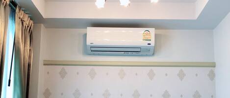 A room with a bed, a ceiling fan, an air conditioner, and a telephone.