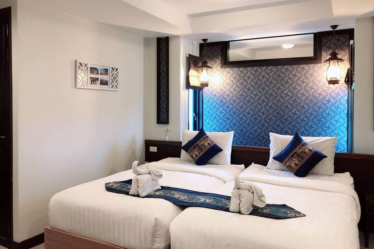 Una habitación de hotel con una cama grande, dos lámparas fijadas a la pared y un papel tapiz estampado.