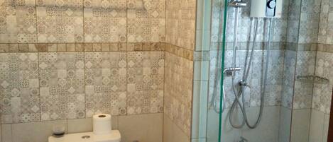 Un baño con inodoro, ducha con mampara de vidrio y azulejos estampados.