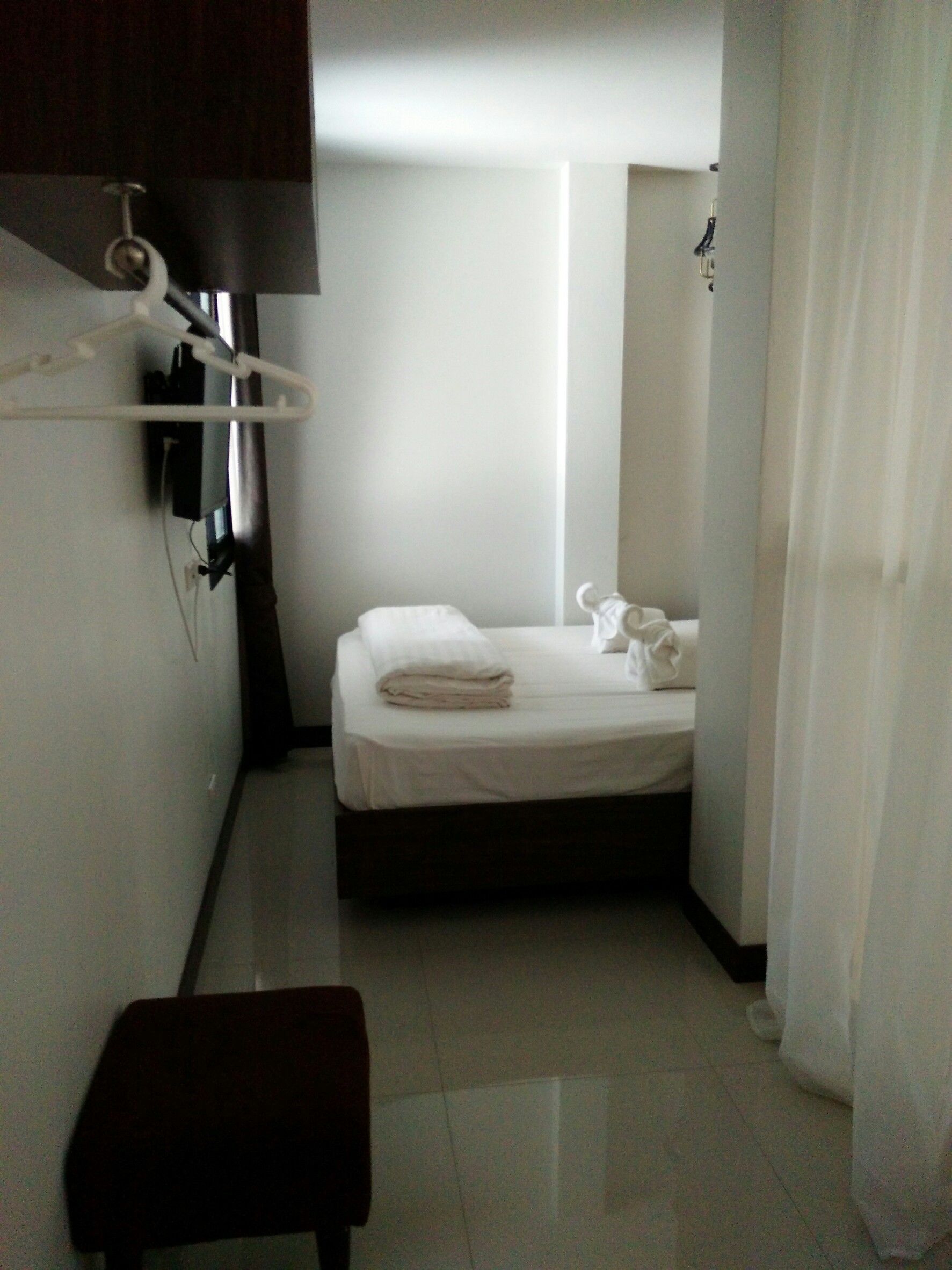 Una habitación de hotel pequeña y limpia, con una cama, un banco y un televisor de pared.
