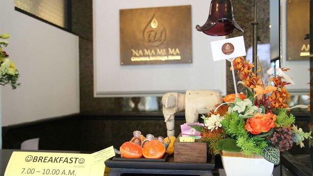 A breakfast setup with a sign indicating 7:00-10:00 A.M. breakfast hours, a bell, a flower arrangement, and a small statue. - Namamema Boutique Hotel (Chiang Mai)