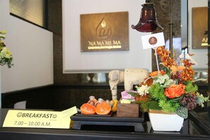 A breakfast setup with a sign indicating 7:00-10:00 A.M. breakfast hours, a bell, a flower arrangement, and a small statue. - Namamema Boutique Hotel (Chiang Mai)