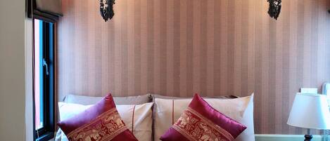 A hotel room with a bed, two decorative pillows, a nightstand with a lamp, and a wall-mounted TV.