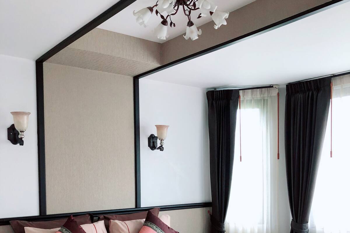 Una cama bien hecha, con una combinación de colores rosa y marrón, un espejo grande encima de la cama y una lámpara en el techo.