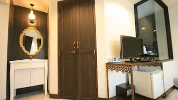 Una habitación con un tocador blanco, una puerta de madera oscura, un espejo grande y una pequeña mesa con un televisor.
