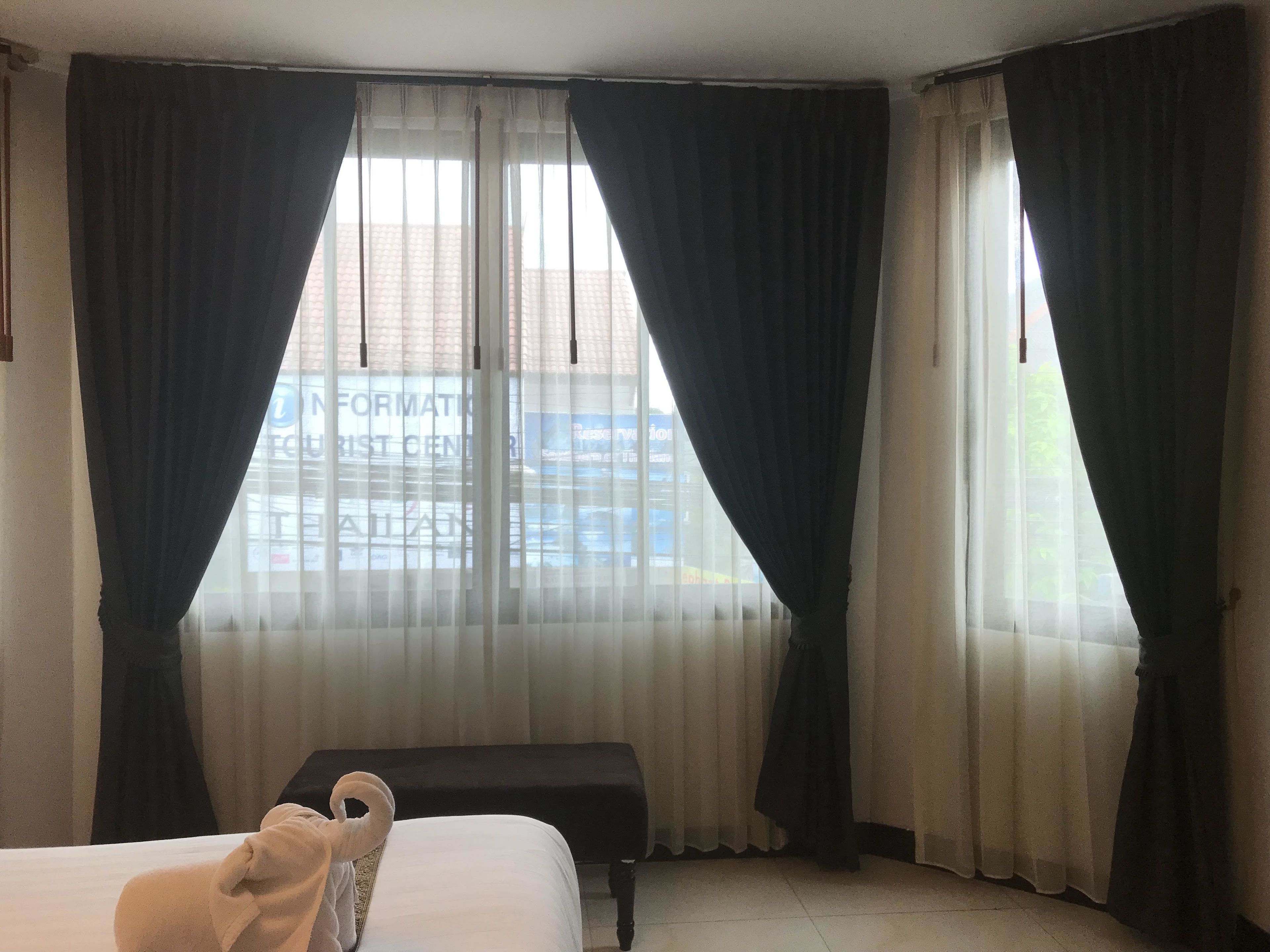 A hotel room with a bed, a bench, and large windows with curtains.