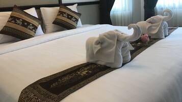 Habitación de hotel con una cama bien hecha, dos toallas con forma de elefantes y un corredor decorativo.
