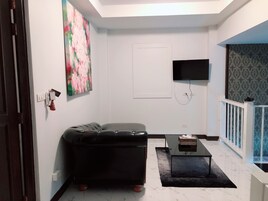 A modern living room with a black leather sofa, a flat-screen TV mounted on the wall, and a small coffee table.