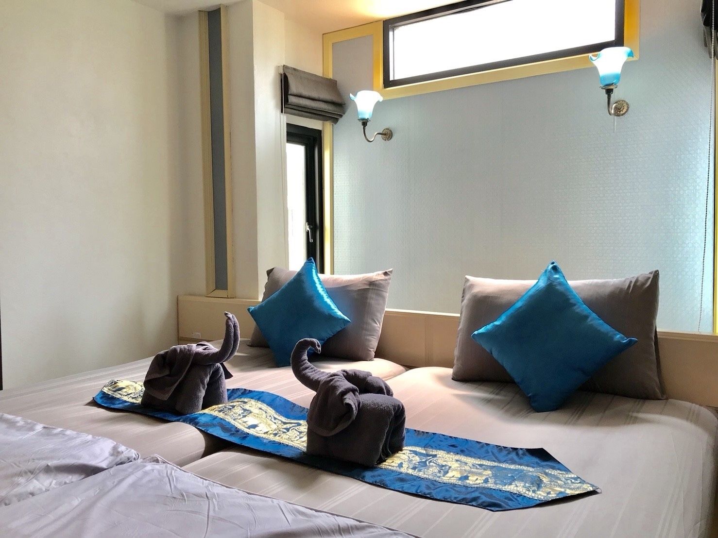A hotel room with a bed, pillows, a window, and a wall-mounted air conditioning unit.
