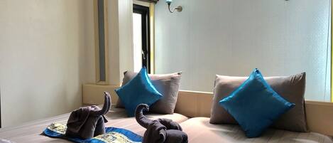 A hotel room with a bed, pillows, a window, and a wall-mounted air conditioning unit.