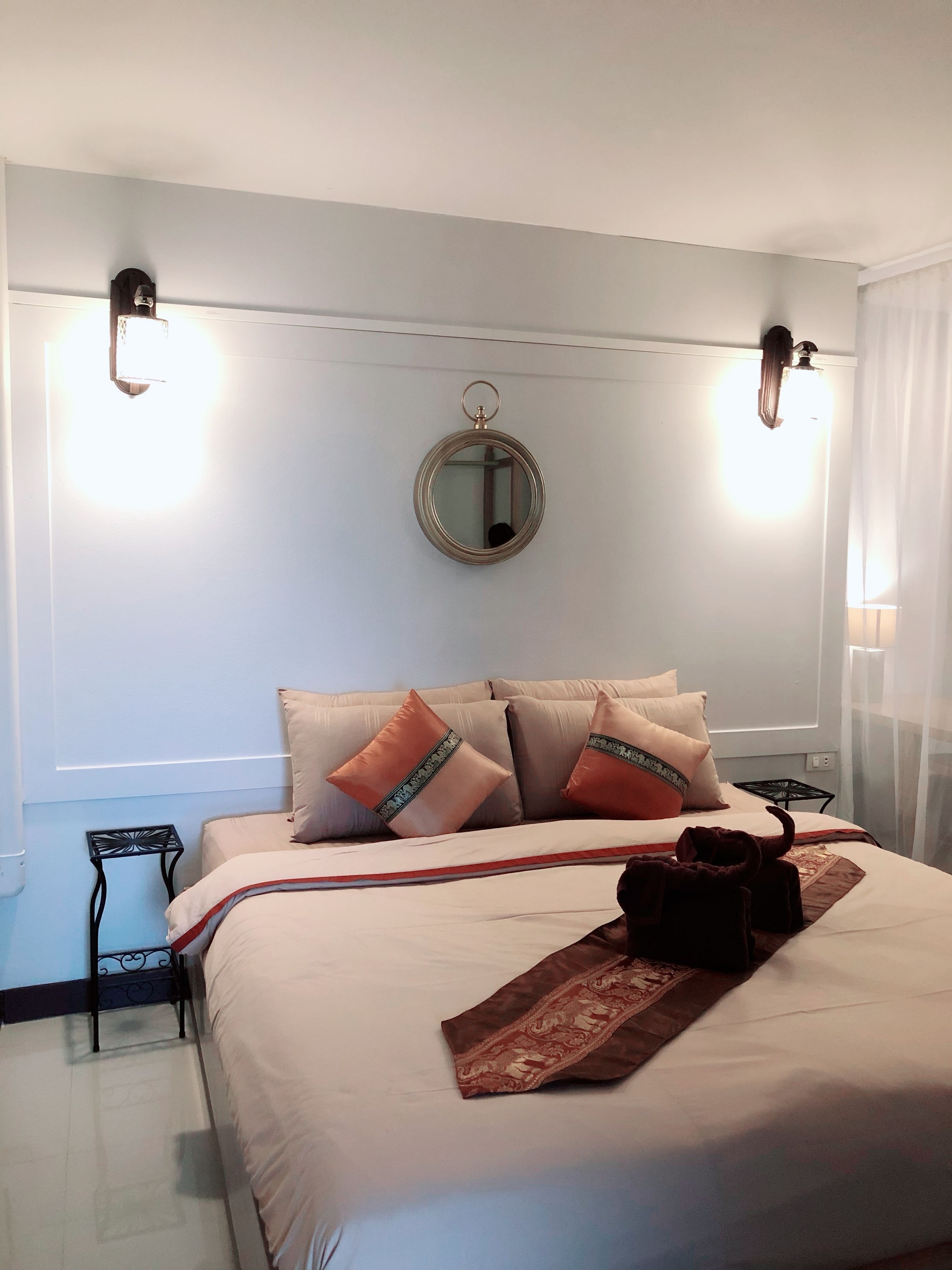 A neatly made bed with a decorative pillow, a bedside table, and a wall-mounted mirror.