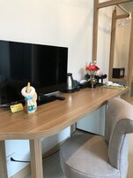 A wooden desk with a television, a remote control, a small decorative item, and a chair.