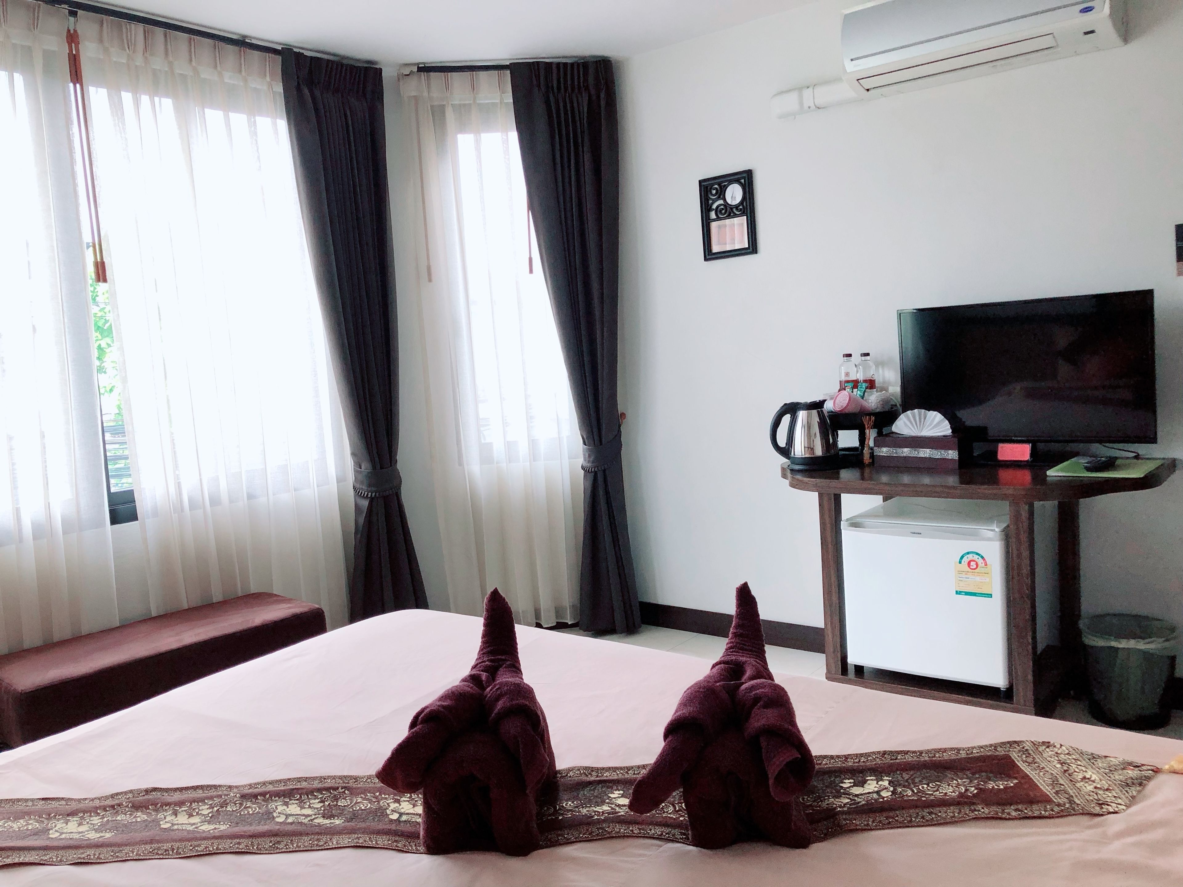 A hotel room with a bed, a TV, a small table with a kettle, and a refrigerator.