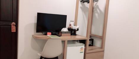 A compact room with a wooden desk, a television, a small refrigerator, and a chair.