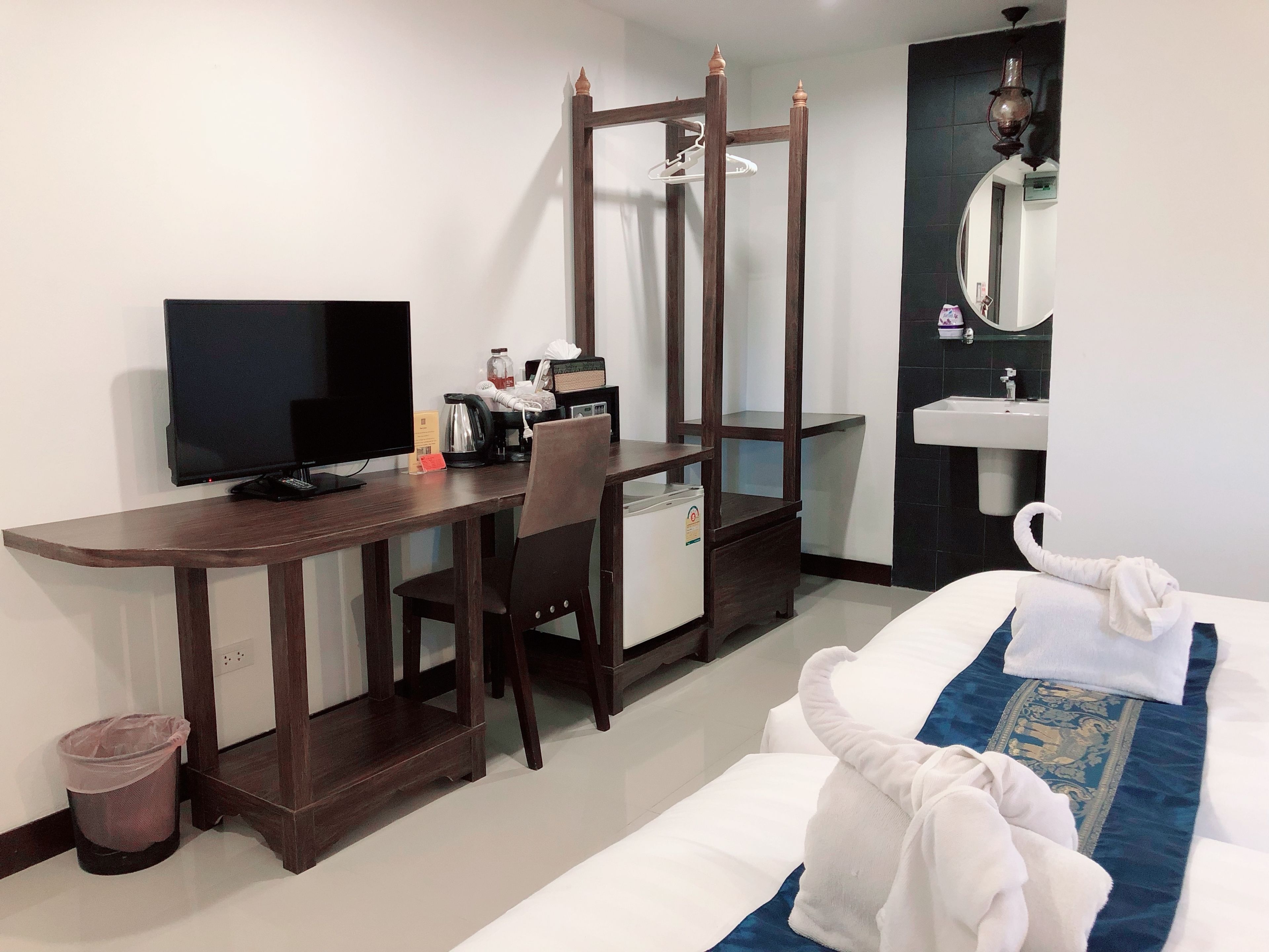 A hotel room with a wooden desk, a television, a minibar, a bed with a blue and white bedspread, a mirror, and a sink.