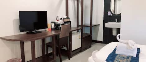 Une chambre d’hôtel avec un bureau en bois, une télévision, un minibar, un lit recouvert d’une courtepointe bleue et blanche, un miroir et un lavabo.