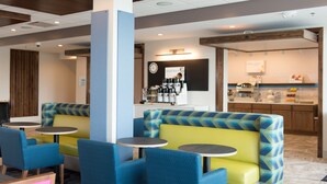 Un restaurant moderne avec des banquettes bleues et jaunes, un bar à café et un comptoir où sont présentés divers plats.