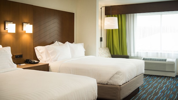 Een hotelkamer met twee bedden, een nachtkastje met een telefoon, een lamp en een raam met gordijnen.
