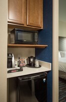 Una kitchenette compacta con microondas, cafetera y refrigerador pequeño.