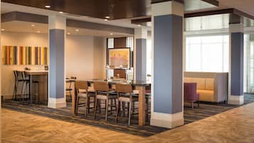 Un hall d'hôtel comprenant un espace repas, un comptoir d'accueil et un coin salon avec un canapé à motifs.