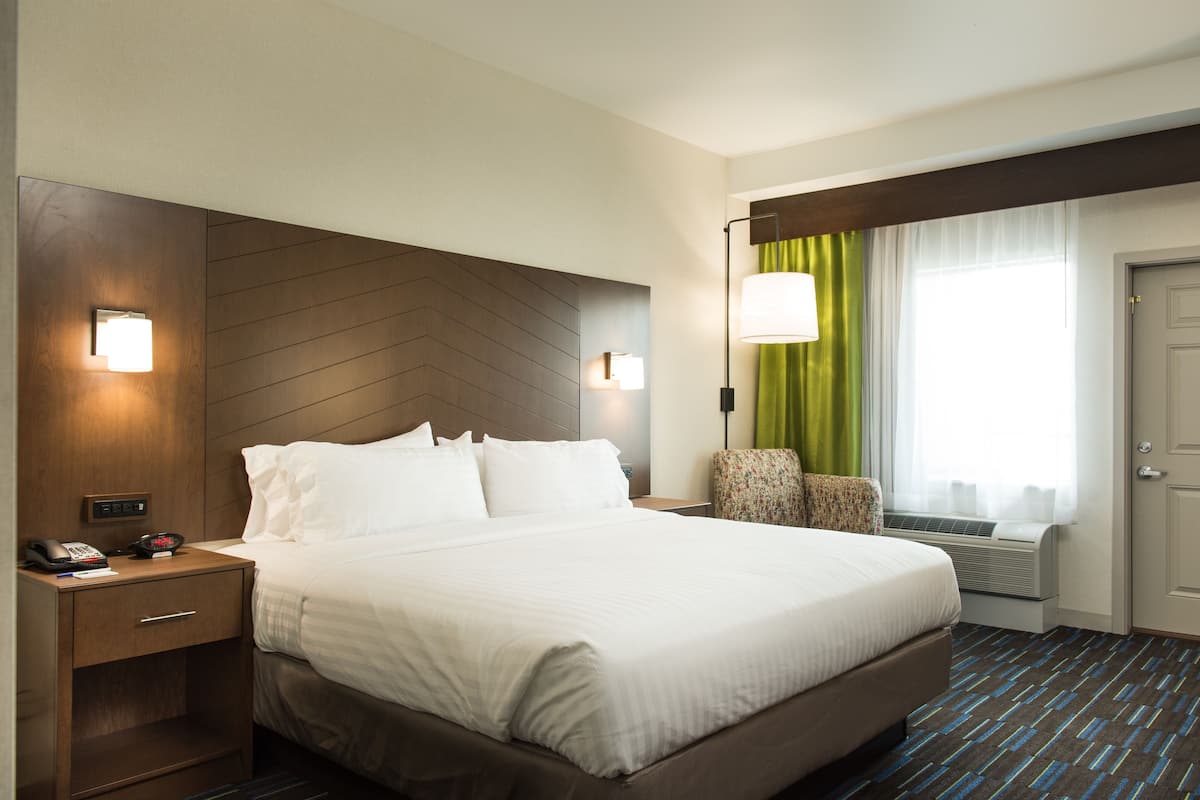 A hotel room with a large bed, bedside tables, a lamp, a chair, and a window with curtains.