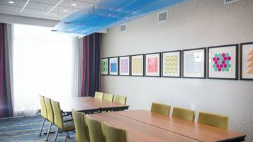 Un salón de conferencias con una larga mesa y sillas, obras de arte enmarcadas en la pared y una ventana con cortinas.