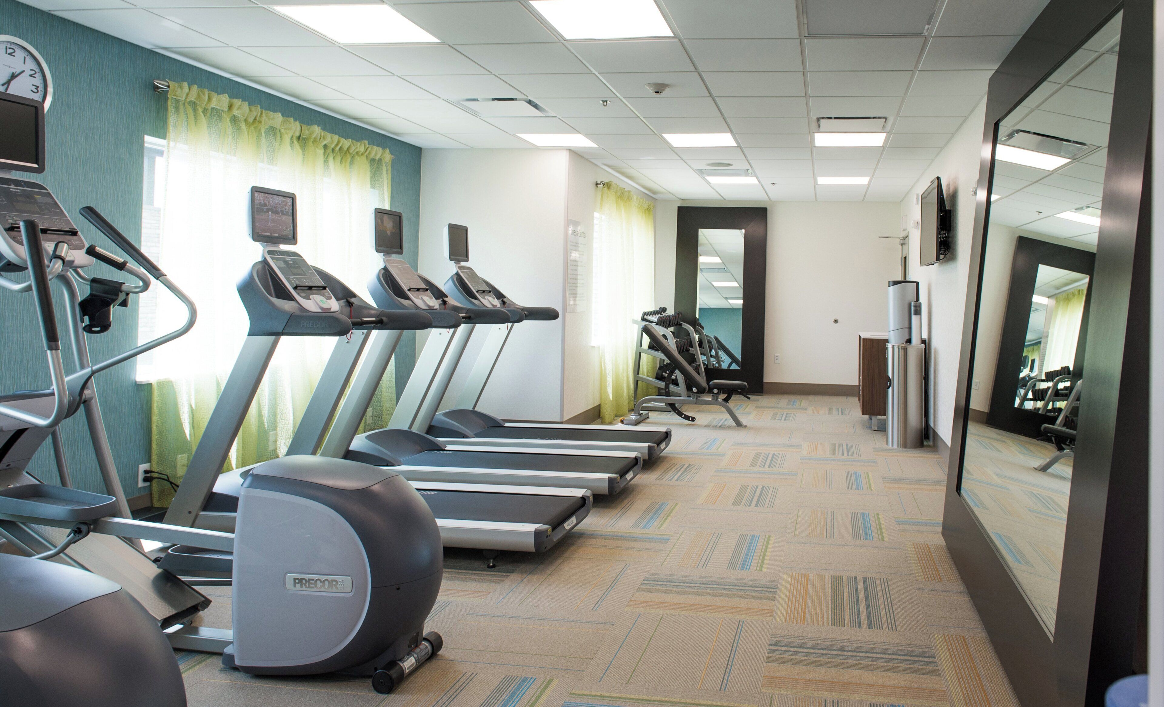 A gym with treadmills, exercise bikes, and a mirrored wall.