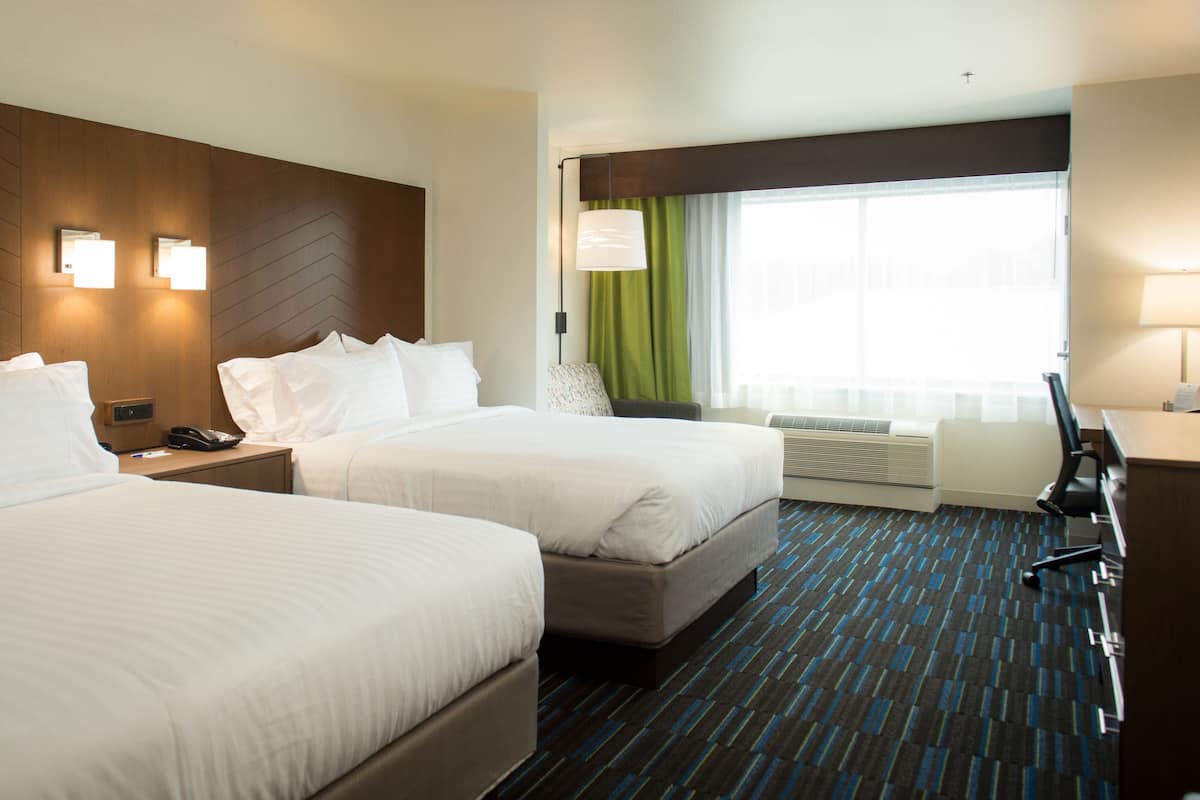 A hotel room with two beds, a desk, a chair, a phone, and a window with curtains.