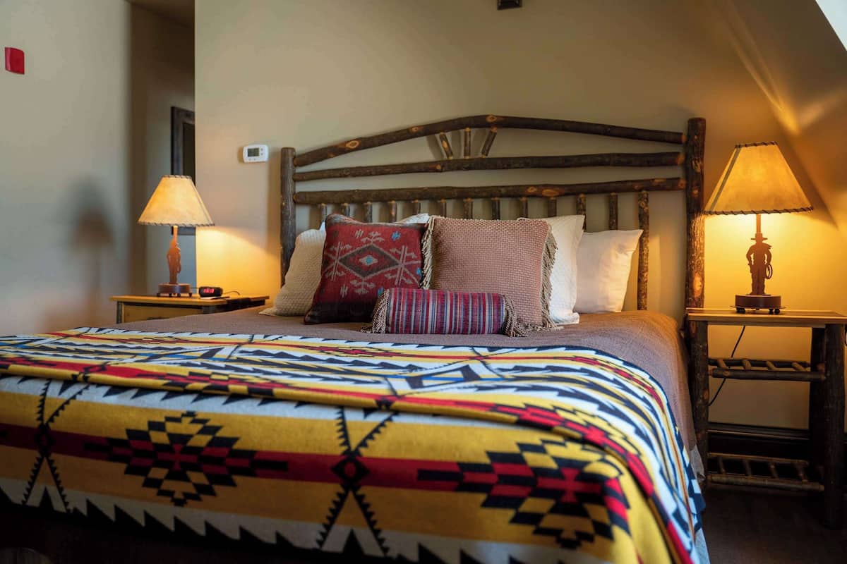A bed with a colorful blanket, two bedside tables with lamps, and a wooden headboard.