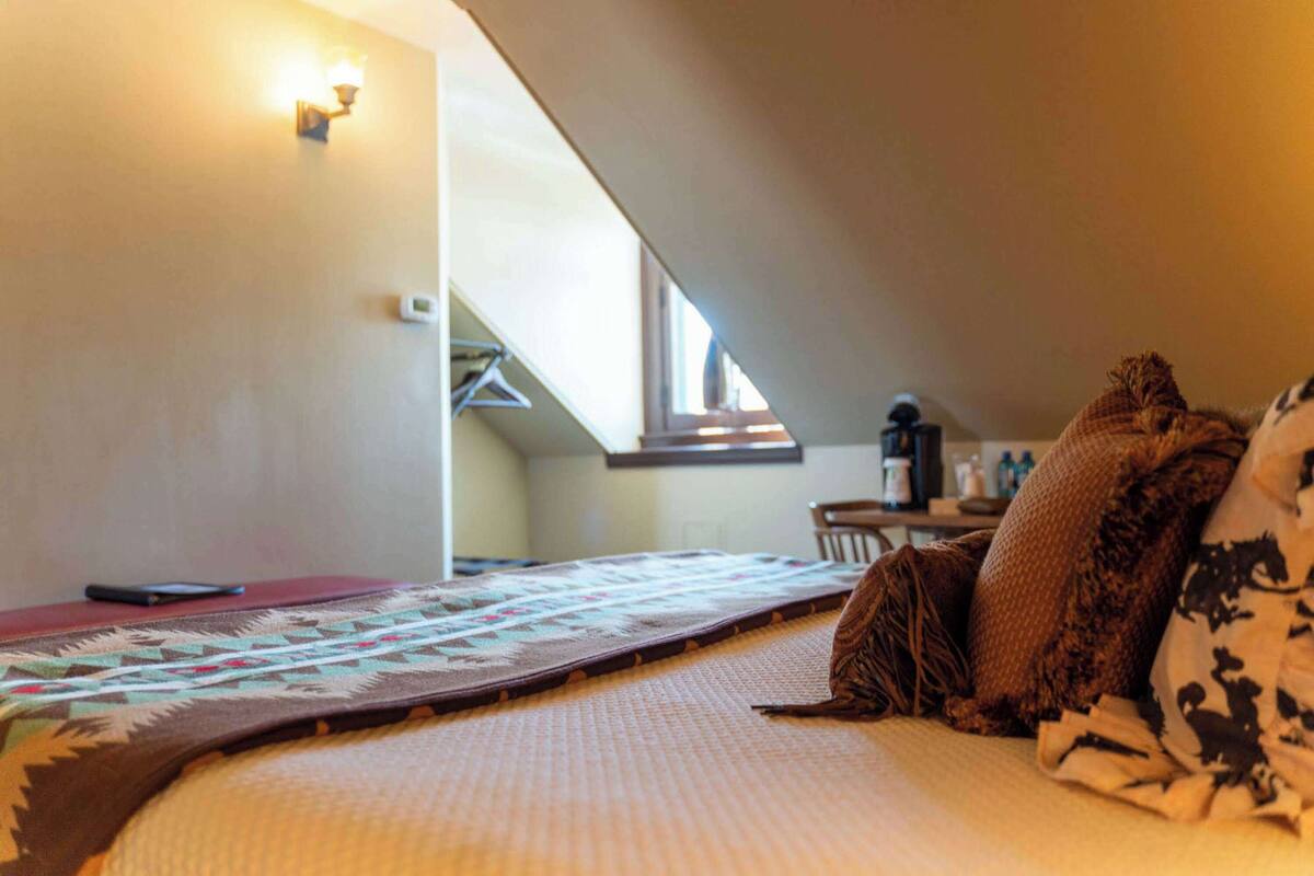 A cozy room with a bed, a quilt, pillows, a wall-mounted lamp, and a window.