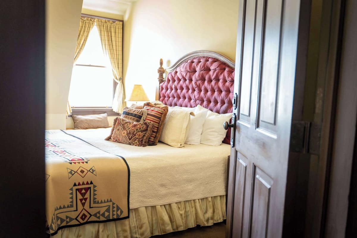 A neatly made bed with a patterned bedspread, a decorative headboard, and a window with curtains.