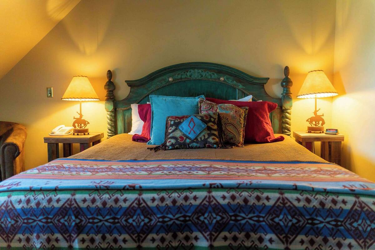 A neatly made bed with patterned bedding, two bedside lamps, and a telephone on a nightstand.