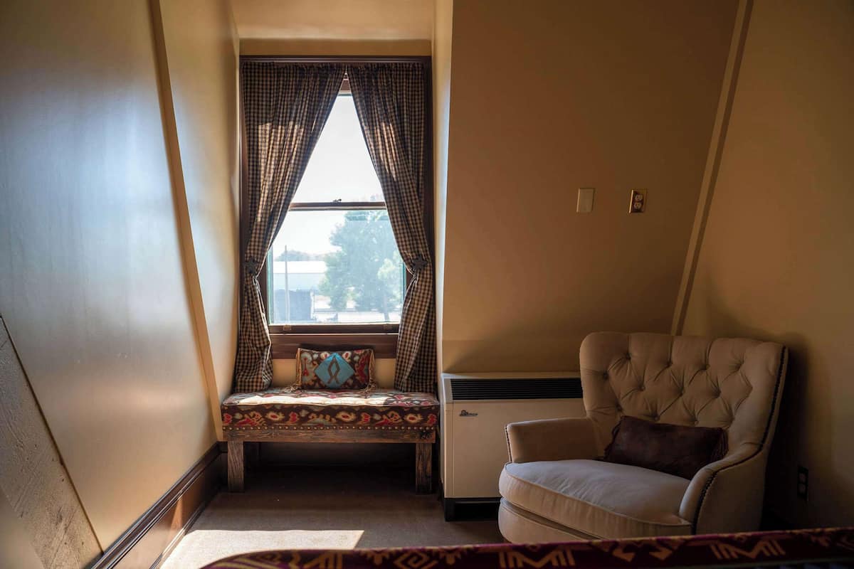 A corner room with a bed, a chair, and a window with curtains.