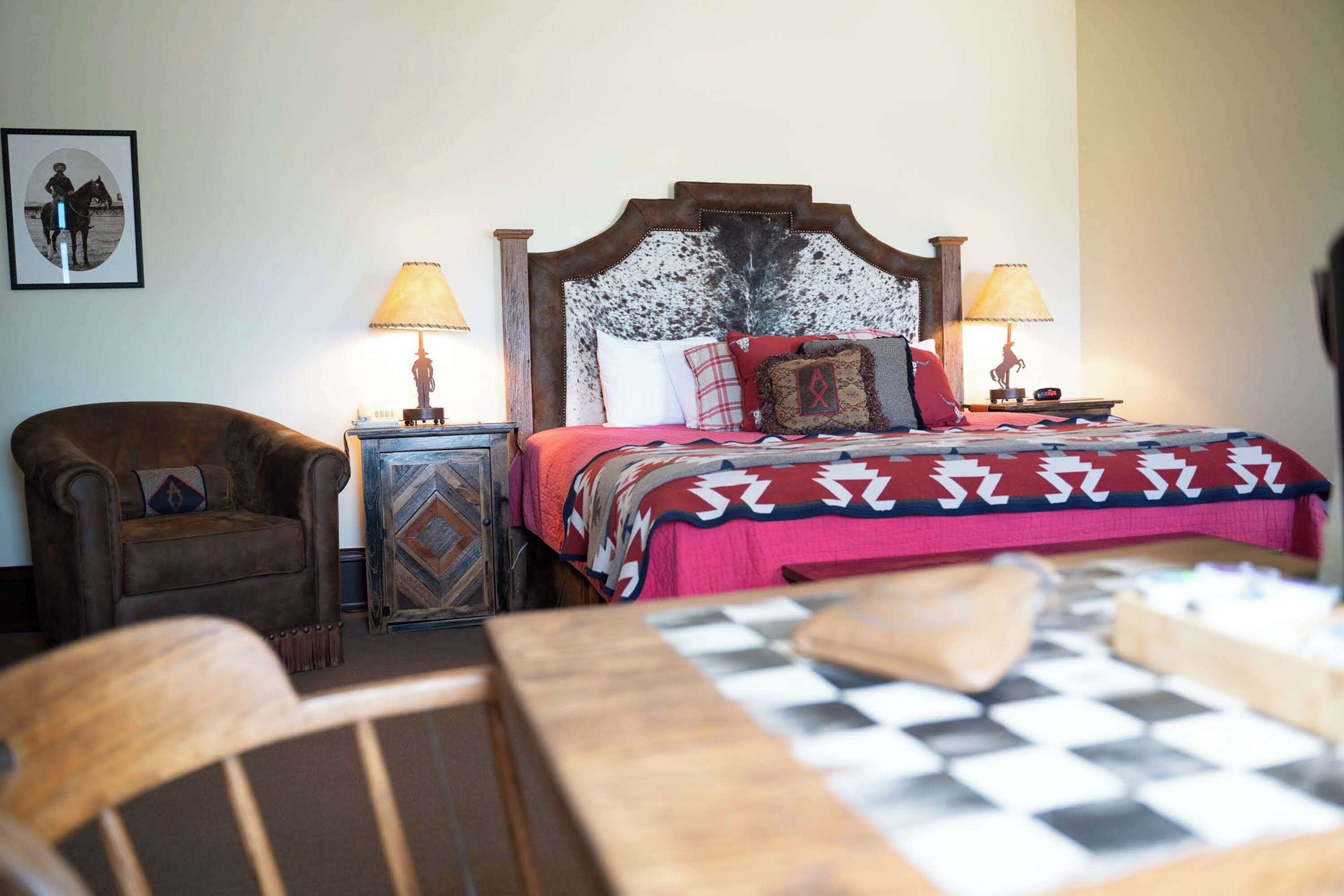 Une chambre à coucher avec un grand lit, deux tables de chevet avec des lampes, une chaise et un élément décoratif mural.