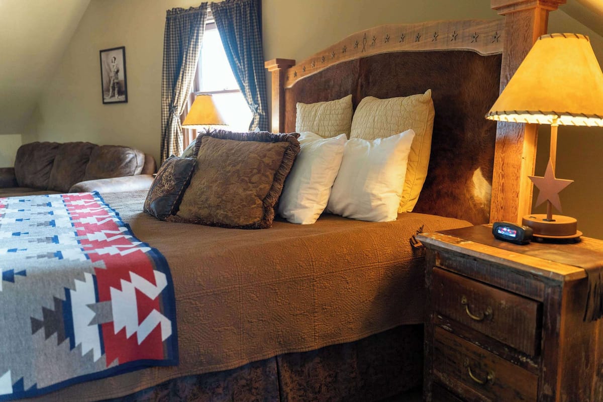 A cozy bedroom with a bed, a nightstand, a lamp, and a window with curtains.