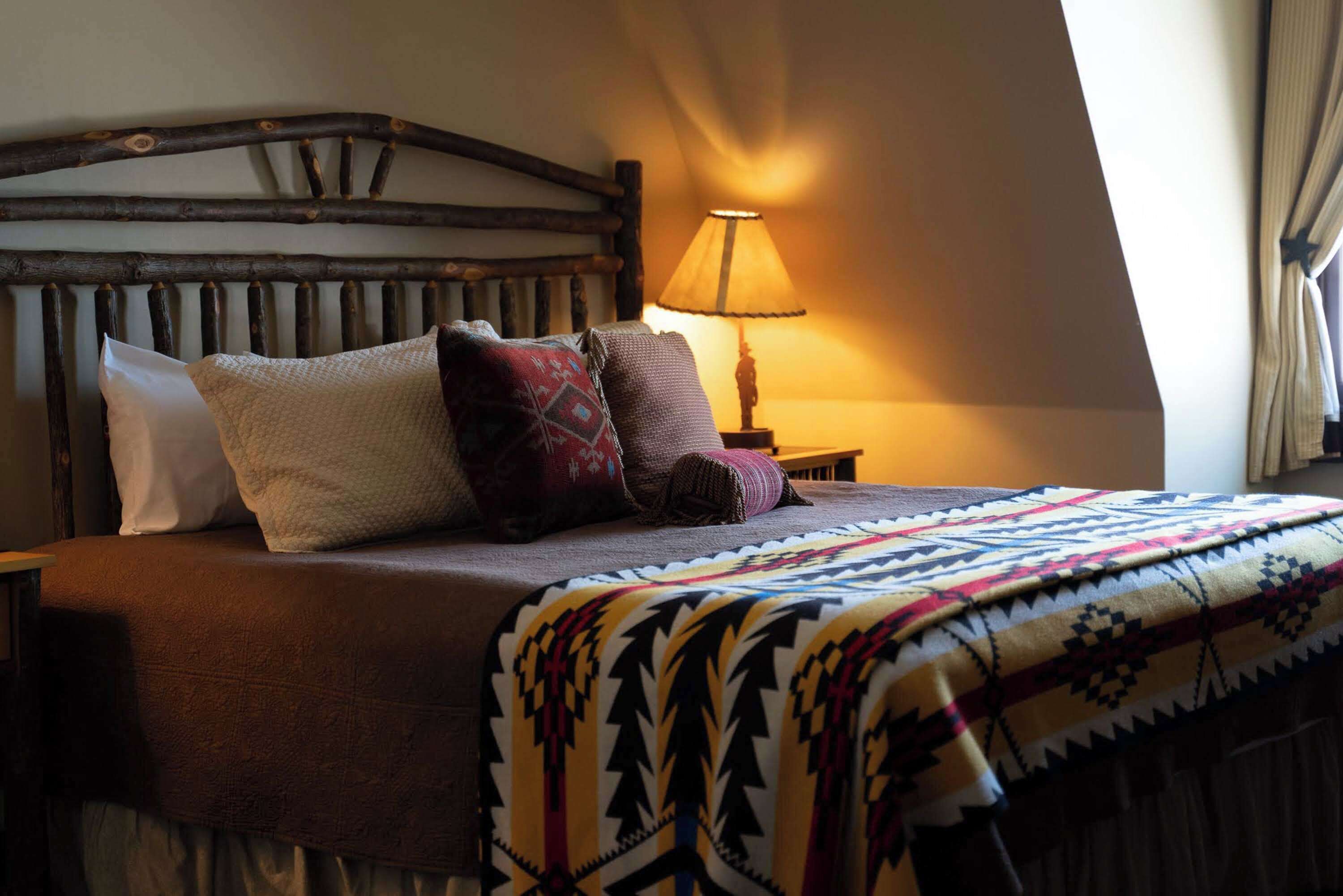 Un lit avec une couverture à motifs, une tête de lit en bois et une lampe de chevet.