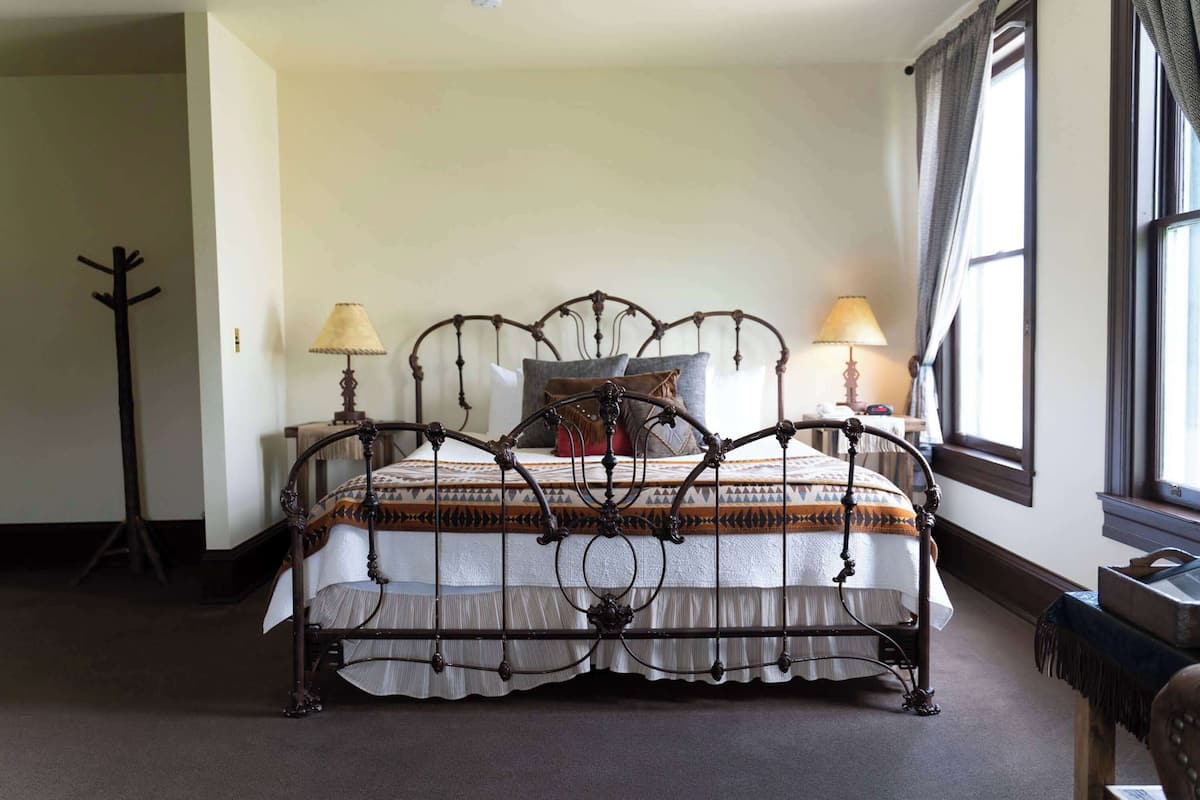 A bed with a metal frame, two bedside lamps, a window with curtains, and a coat rack.