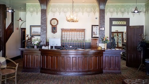A reception area with a wooden reception desk, a clock, and a patterned wall. - Sheridan Inn, B/W Signature Collection (Sheridan)