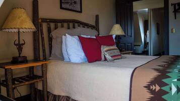 A bed with a wooden headboard, a beige blanket, and a patterned throw. There are two bedside tables with lamps.